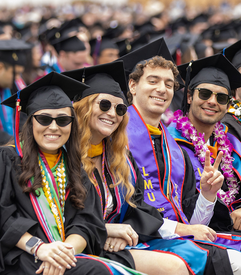 four students wearing their cap and gown at commencement